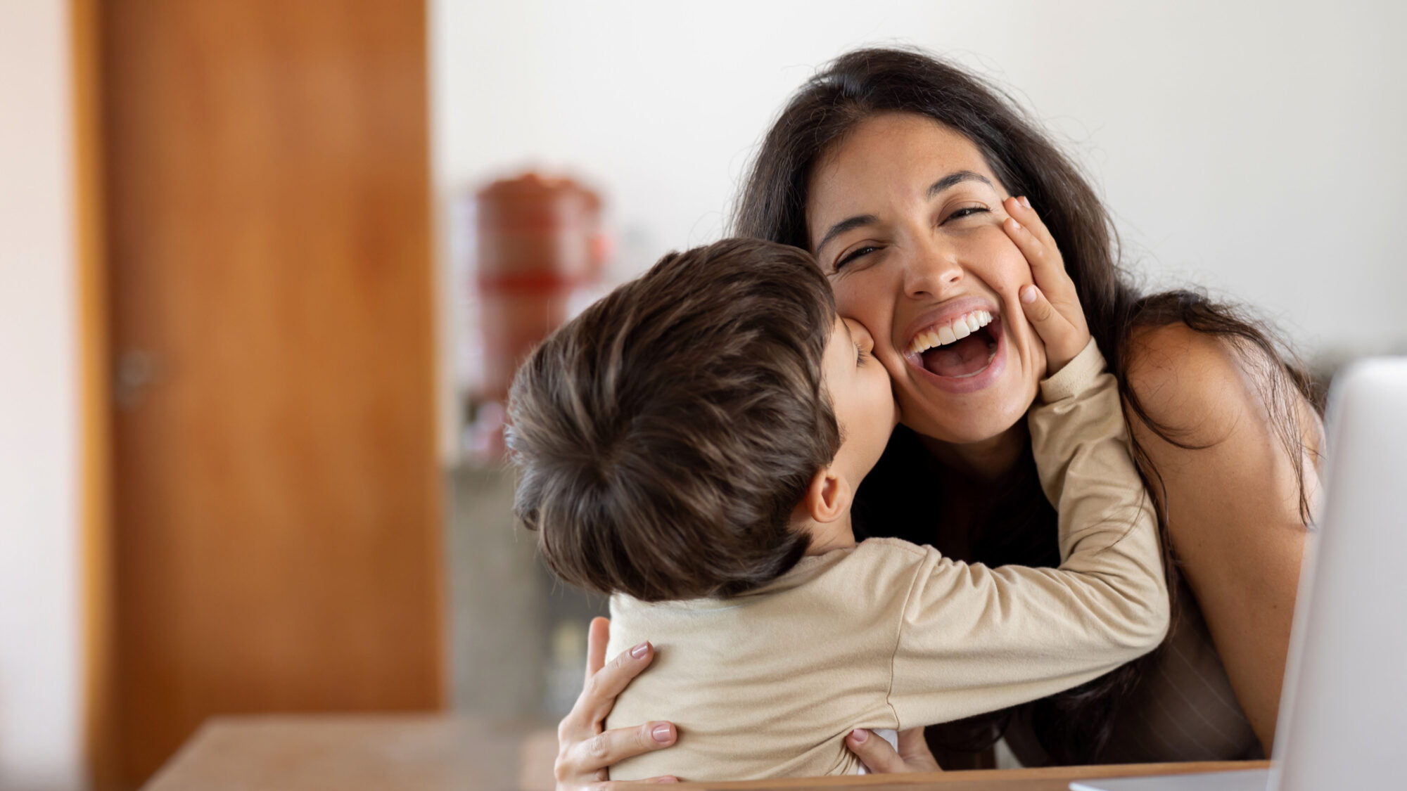 Loving son giving a kiss to her mother while she is working at home