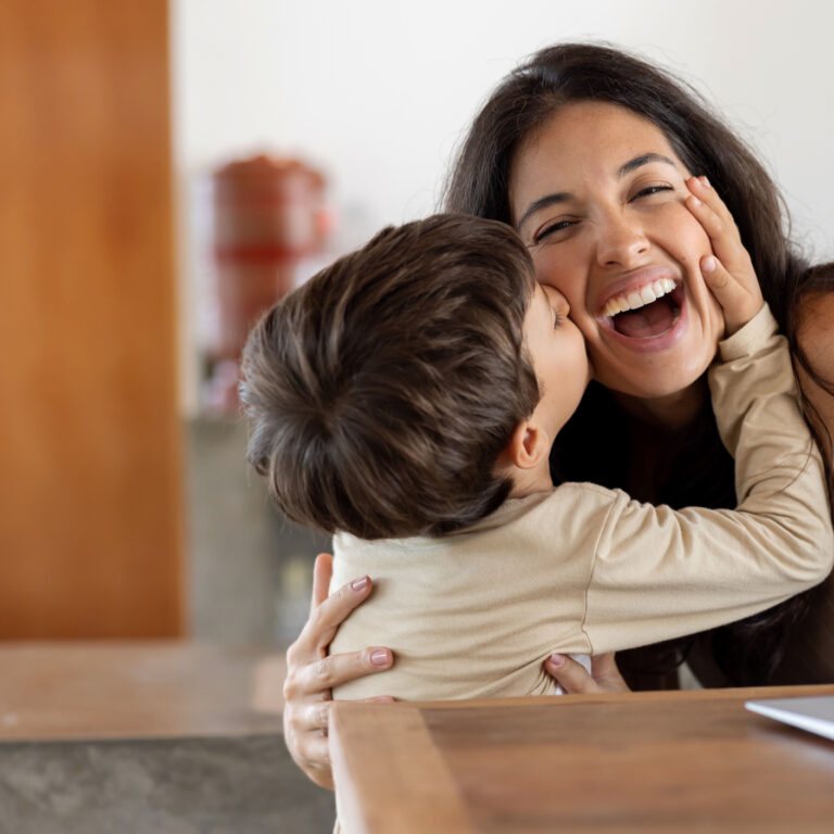 Loving son giving a kiss to her mother while she is working at home
