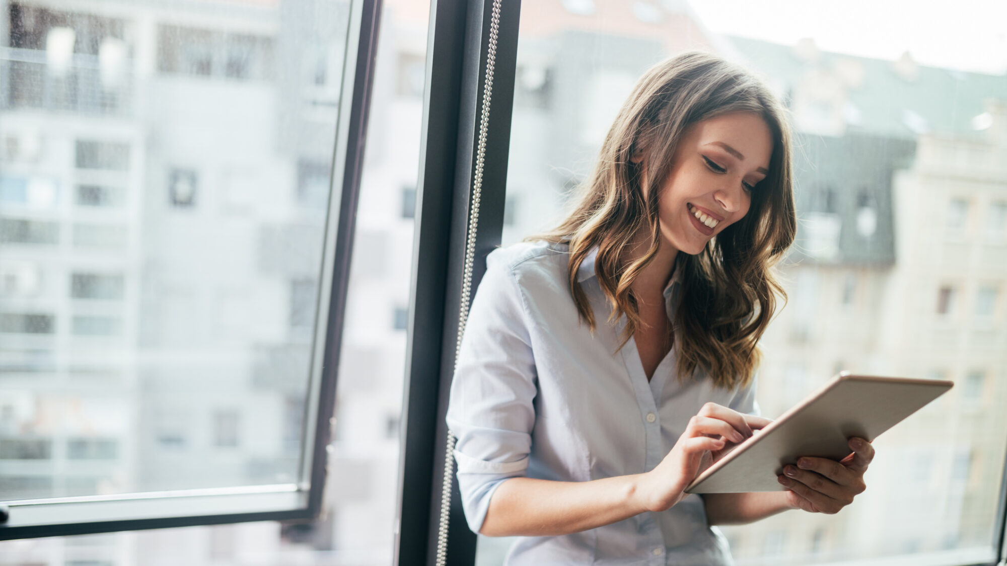 Attractive businesswoman using a digital tablet while standing in front of windows
