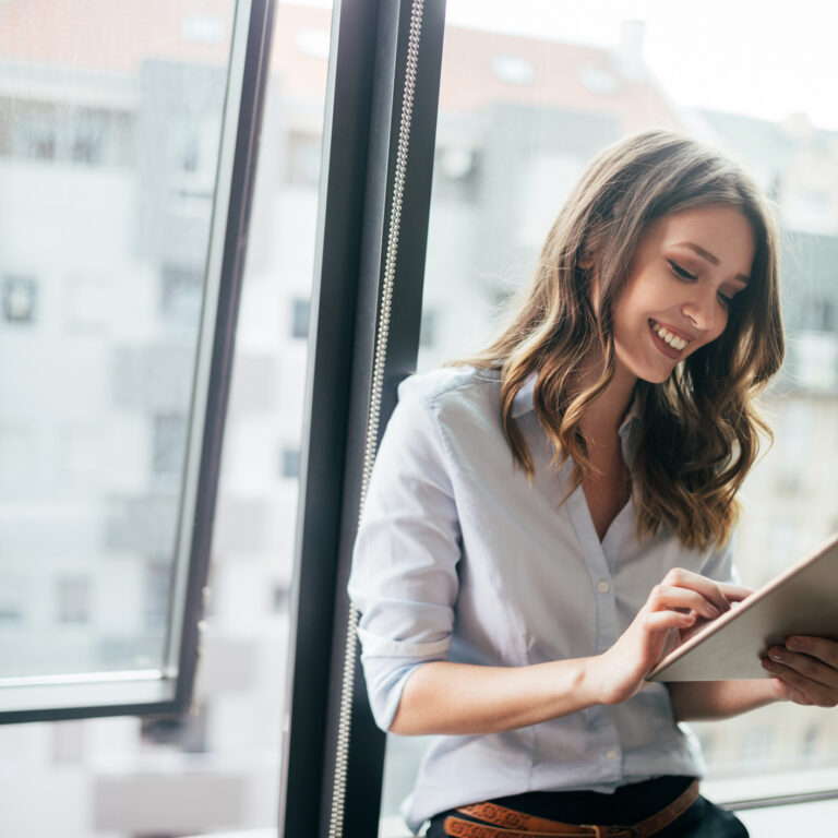 Attractive businesswoman using a digital tablet while standing in front of windows